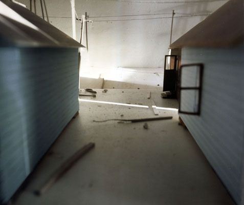 Steht man im Raum, ist man umgeben von einer kleinen verlassenen Siedlung. Diese Siedlung habe ich zuerst als Modell gebaut um darin die vier Aufnahmen - in jede "Himmelsrichtung" machen zu können. Danach wurden die Fotografien auf Raumhöhe vergrössert und die vier Wände der Ausstellungskoje damit beklebt.