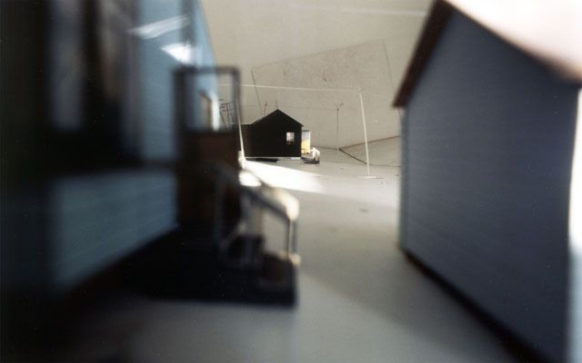 Steht man im Raum, ist man umgeben von einer kleinen verlassenen Siedlung. Diese Siedlung habe ich zuerst als Modell gebaut um darin die vier Aufnahmen - in jede "Himmelsrichtung" machen zu können. Danach wurden die Fotografien auf Raumhöhe vergrössert und die vier Wände der Ausstellungskoje damit beklebt.