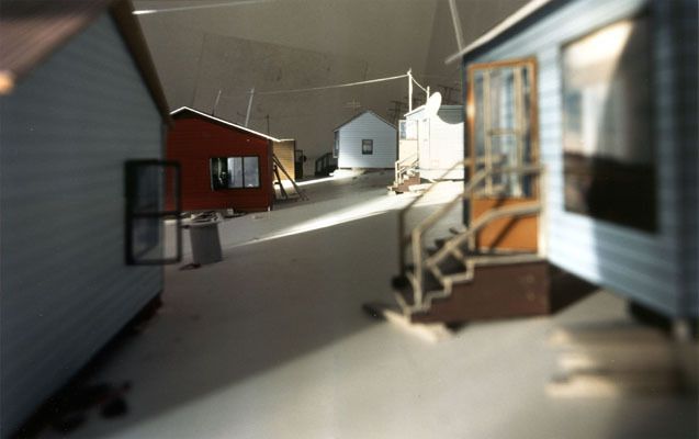 Steht man im Raum, ist man umgeben von einer kleinen verlassenen Siedlung. Diese Siedlung habe ich zuerst als Modell gebaut um darin die vier Aufnahmen - in jede "Himmelsrichtung" machen zu können. Danach wurden die Fotografien auf Raumhöhe vergrössert und die vier Wände der Ausstellungskoje damit beklebt.