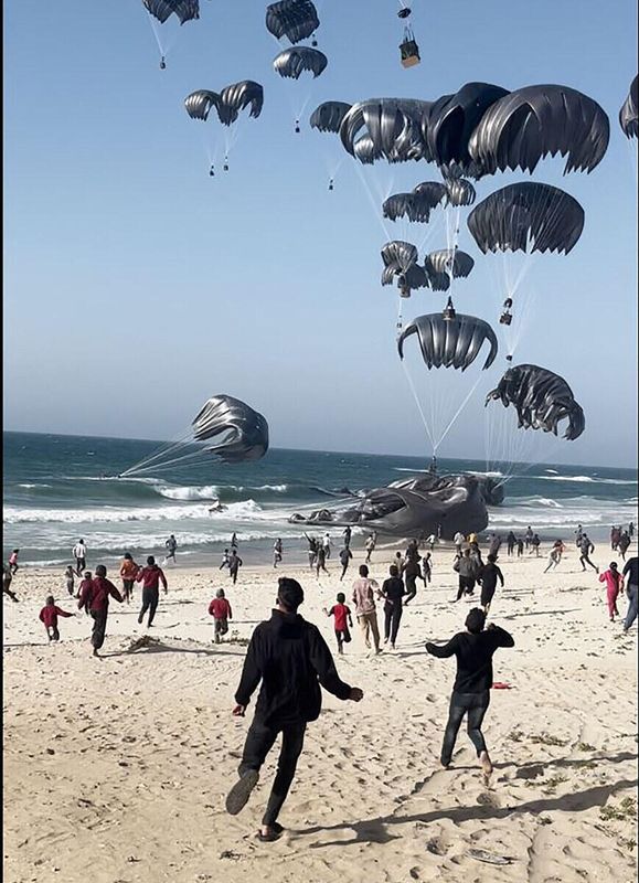 Dieses Bild aus einem AFPTV-Video zeigt Palästinenser, die auf Fallschirme zu rennen, die an Lebensmittelpaketen befestigt sind, die von US-Flugzeugen am 2. März 2024 an einem Strand im Gazastreifen abgeworfen wurden. (AFP)